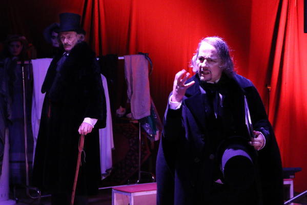 Charles Dickens spricht über seine Weihnachtsgeschichte in der der hartherzigen Geizhals Ebenezer Scrooge (Im Hintergrund) von den Geistern der Weihnacht auf den richtigen Weg geführt wird  (alle Figuren werden dargestellt vom Theaterensemble Faust III). 