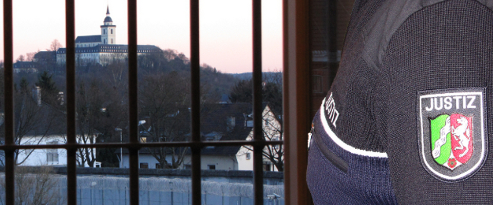 Justizvollzugsbeamter bei der Haftraumkontrolle am Haftraumfenster mit Blick auf den Brückberg.