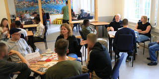 Die Veranstaltung fand statt im Besuchsraum von Haus 2. An den Tischen sitzen zusammen die Vertreter aus den verschiedenen Häusern die Wohnangebote machen mit Inhaftierten aus der JVA.