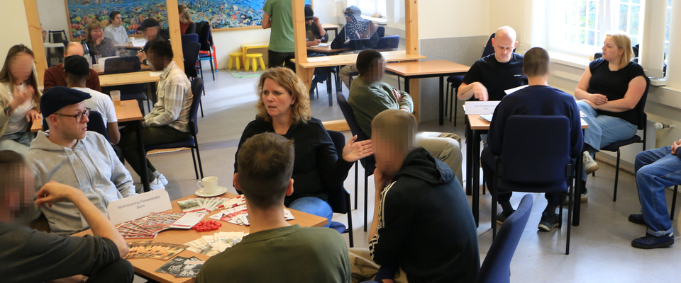 Die Veranstaltung fand statt im Besuchsraum von Haus 2. An den Tischen sitzen zusammen die Vertreter aus den verschiedenen Häusern die Wohnangebote machen mit Inhaftierten aus der JVA.