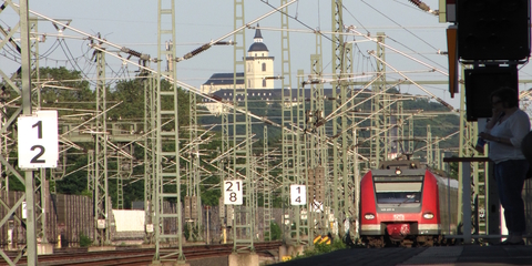 Einfahrt eines Zuges in den Bahnhof Troisdorf. Im Hintergrund ist die Abtei von Siegburg zu sehen.