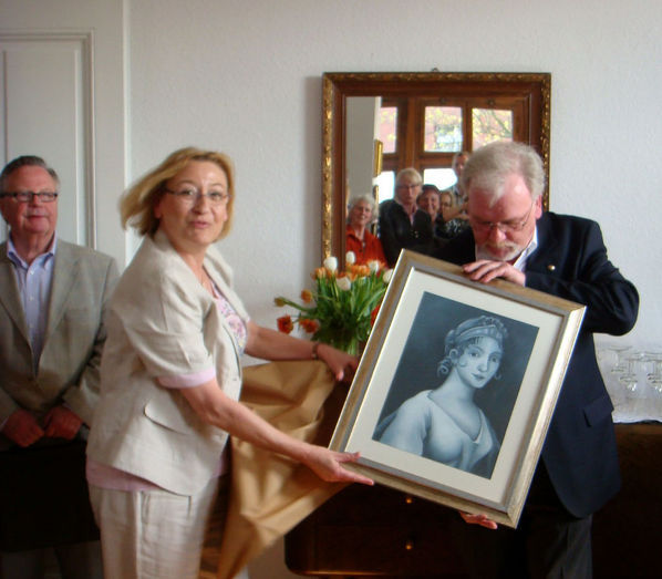 Als Geschenk überreicht Herr Werner Kaser stellvertretend für einen Inhaftierten dessen gemaltes Bild der preußischen Königin Luise, die Namensgeberin für das Café ist, an die Sprecherin der Ehrenamtlichen Frau Maria Braun-Schmitz zur Ausgestaltung des Café.