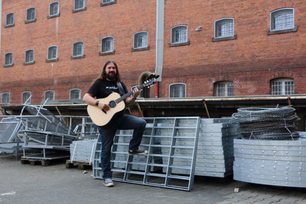 Mr. Tottler steht mit seiner Gitarre im Küchenhof der Justizvollzugsanstalt Siegburg. Im Hintergrund der sogenannte A-Flügel von Haus 1.