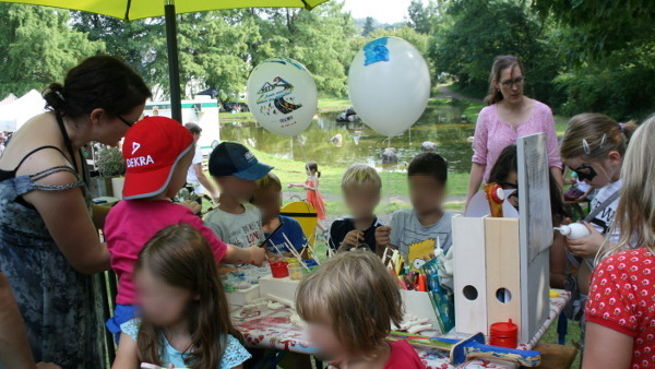 Kinder malen und basteln in der Kinderwerkstatt mit dem Spielplatzteich im Hintergrund.