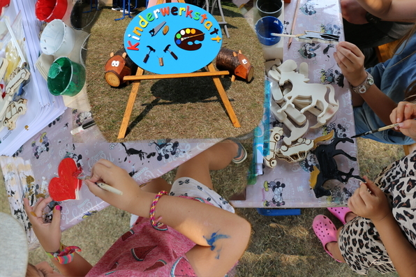 Kinder beim malen. In der Mitte das Werbeschild für die Kinderwerkstatt, flankiert von zwei "Wildschweinen", die als Dekorationsartikel in der Arbeitstherapie Holz hergestellt wurden. 